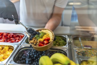 Person wearing gloves preparing a nutritious acai smoothie bowl, adding fresh blueberries, sliced
