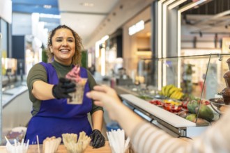 Young female entrepreneur serving a freshly prepared frozen yogurt cup to a customer, representing