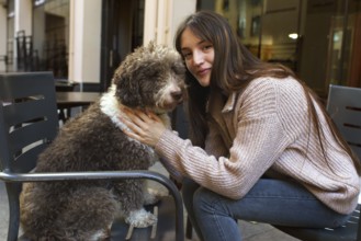 A young woman with long hair and a cozy sweater lovingly embraces her fluffy brown and white dog
