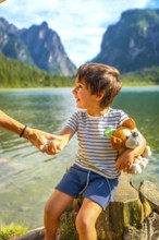 Smiling child holding a plush toy and his parent's hand while enjoying a summer day at lake