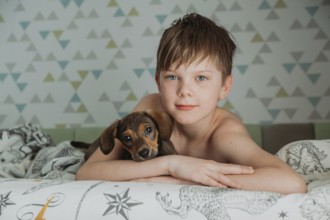 A young boy, with thoughtful blue eyes, gently holds his small Dachshund puppy as they relax