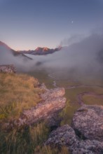 A breathtaking mountain landscape at dawn, with a rocky foreground, misty valley, winding stream,