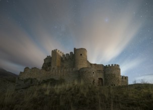 Night falls over the Manqueospese Castle in Avila, Spain, with star trails shimmering above its