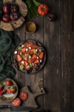 Anonymous people preparing a healthy tomato and strawberry salad on a wooden rustic table