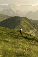 A man pauses to rest on a stunning mountain trail, surrounded by lush green hills under a serene
