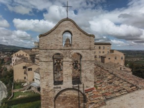 A historic bell tower stands amid rustic rooftops in Treia, Italy. The brick architecture contrasts