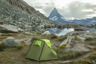 A vibrant green tent is set by a tranquil alpine lake, with the majestic Matterhorn towering in the