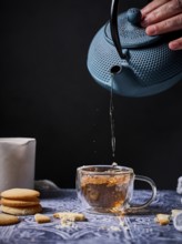 A serene setup of afternoon tea featuring a blue teapot pouring tea into a glass cup, accompanied