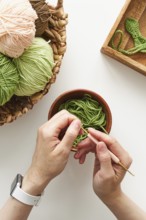 Top view of cropped unrecognizable hands crocheting with a pink hook and green yarn in a creative