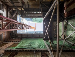 Looking up inside a building under construction, steel beams, scaffolding, and a towering crane
