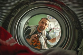 Man loads laundry, looking into washer from inside drum, home chore scene