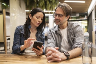 A couple sits at a wooden table, engaged in a lively conversation while sharing something on a
