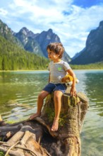 Young boy sitting on a tree stump by lake dobbiaco, holding his plush toy and admiring the