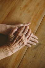 Close-up of elderly hands gently resting on a wooden table, capturing the texture and warmth of