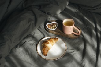 A golden homemade croissant rests on a white plate, accompanied by a wooden tray holding a pink cup