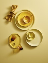 Top view of a stylish yellow ceramic crockery set, including plates, bowls, cups, and a golden