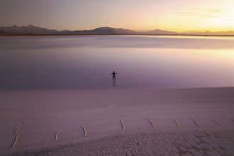 A solitary figure stands in the vast expanse of Salinas Grandes, Salta, Argentina, at sunset. The