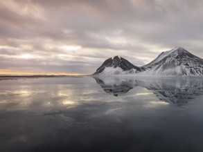 Stokksnes Beach in Iceland showcases stunning winter reflections. Snow-dusted peaks and tranquil