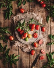 Fresh vine tomatoes are artistically arranged on a rustic wooden table, surrounded by green leaves,