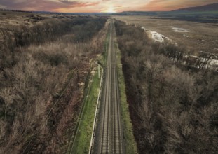 From above, a drone captures the serene landscape of a railway slicing through a barren forest in