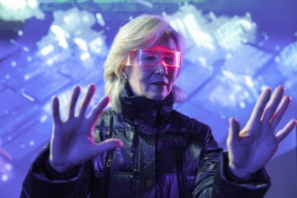 An elderly Asian woman interacts with virtual elements in the metaverse, wearing futuristic glasses