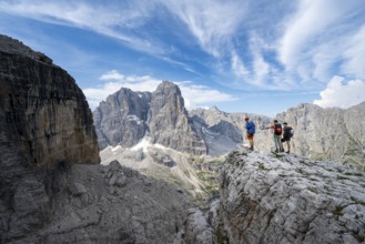 Three mountaineers on a rock in front of a picturesque mountain landscape with rocky peaks, Via