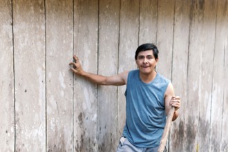 A middle-aged man stands confidently in the Colombian countryside, leaning against a rustic wooden