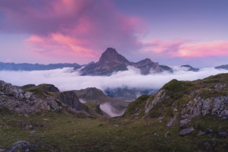 A breathtaking mountain peak surrounded by clouds at sunrise in the Pyrenees. The vibrant pink sky