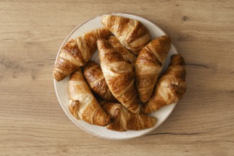 A top view of freshly baked homemade croissants arranged on a white plate, placed on a wooden