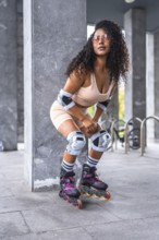 Vertical photo of an urban latin woman posing with inline skates and pink sportive clothes in an