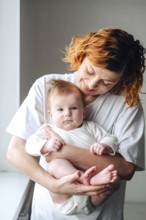 A mother lovingly holds her newborn baby girl, captured in warm natural light. The white clothing