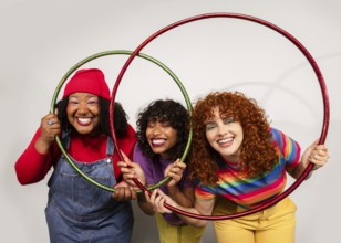 Three women share joyful moments, smiling brightly as they play together with colorful hula hoops.