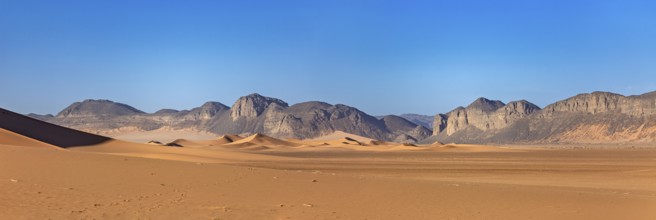 Gentle sand dunes with mountains in the background and a bright blue sky, The landscape of the