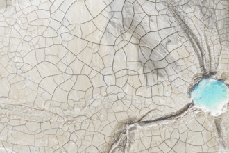 Aerial view of cracked earth with intricate lines and a vibrant blue water body in the corner. This