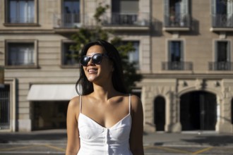 A fashionable Chinese woman in sunglasses and a white dress enjoys a bright summer day in the city,