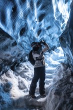 A person is taking a picture in a cave with a backpack on. The cave is filled with ice and snow