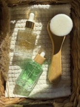 A top down view of two serum cosmetic bottles and a facial brush arranged on a textured surface in