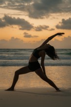 A woman gracefully poses in a yoga stance on a beach during sunset in Tulum, Mexico. The serene