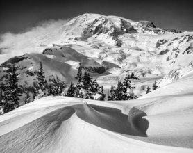 Captivating black and white photo of a mountain landscape blanketed in snow, framed by towering