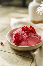 Homemade pink berry mousse garnished with fresh red currants in a ceramic bowl on a tiled table,