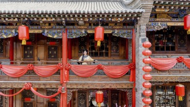 A woman dressed in traditional Qing dynasty clothing stands on a intricately decorated balcony in