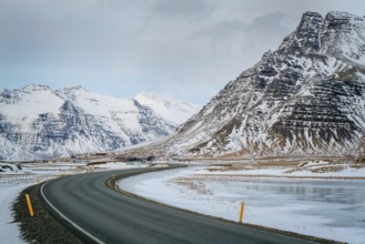 A curved road leads through stunning snowy mountains in Iceland. The winter landscape features