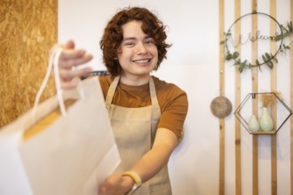 A cheerful shop assistant in an apron hands a paper bag to a customer, creating a warm and