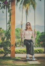 Portrait of a smiling girl sitting on a swing in a nature park. Happy young woman sitting on a
