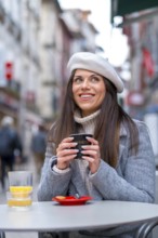 Vertical photo of a chic woman drinking hot coffee in an outdoors cafeteria during a cold day