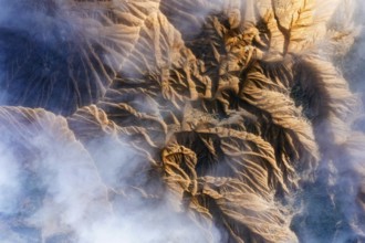 An aerial view showcases rocky mountain formations with deep ridges and valleys Wisps of mist