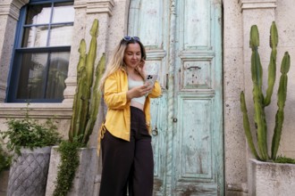 A female tourist stands in front of an ornate wooden door, intently using her smartphone to