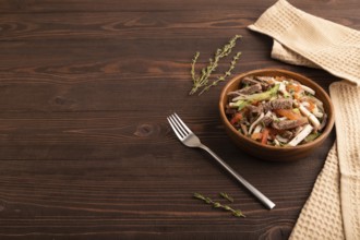 Meat salad with beef and vegetables in wooden bowl on brown wooden background and linen textile.