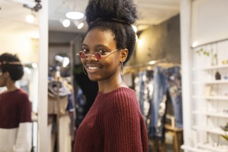 An elegant woman with curly hair tries on a pair of distinctive sunglasses in a fashion store. She