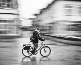 A person on a bicycle rides through a city in bad weather and sleet, rainy day black and white